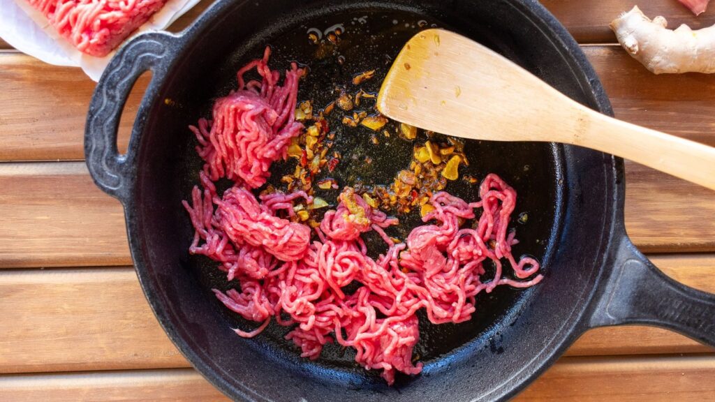 Viande hachée en train de colorer dans une poêle avec des oignons émincés