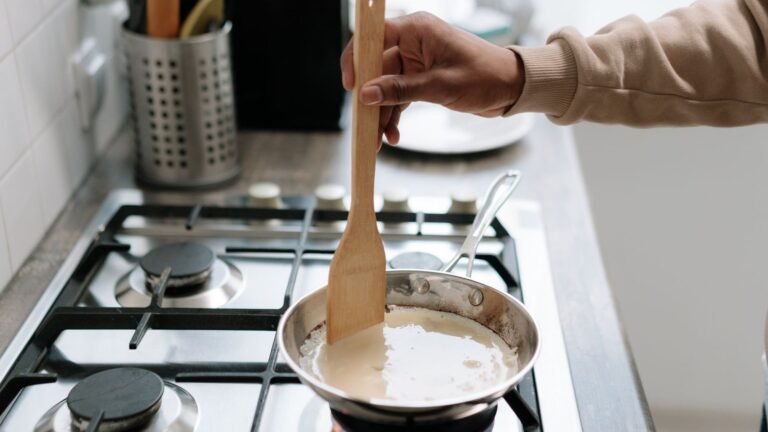 Sauce blanche remuée à la cuillère en bois dans une casserole posée sur une gazinière