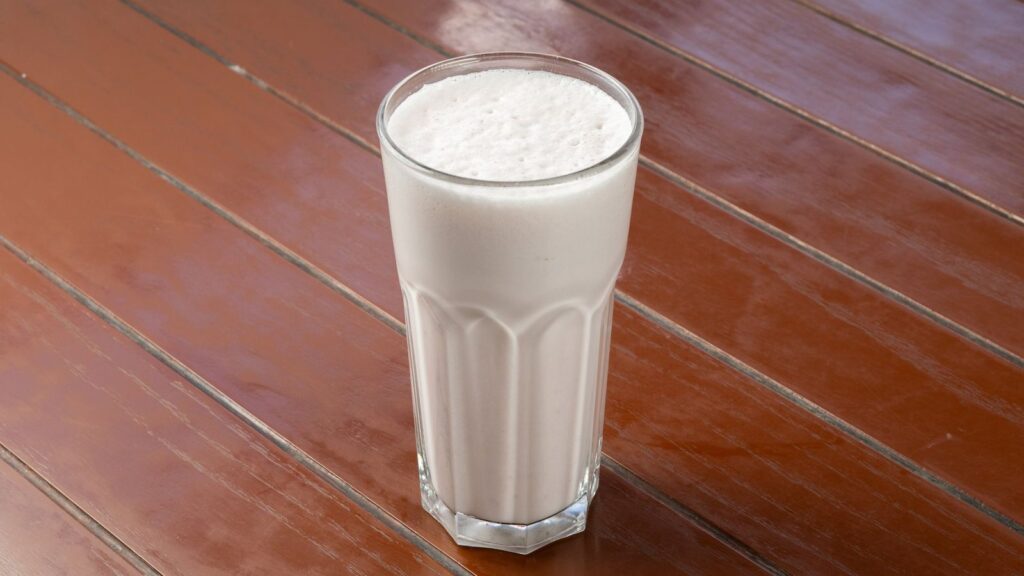 Grand verre de lait entier sur une table en bois, prêt à être tiédi pour la sauce
