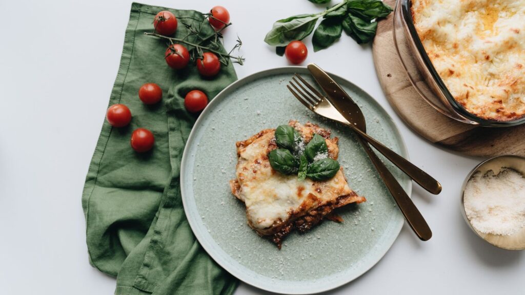 Part de lasagnes servie dans une assiette, le plat de cuisson posé à côté