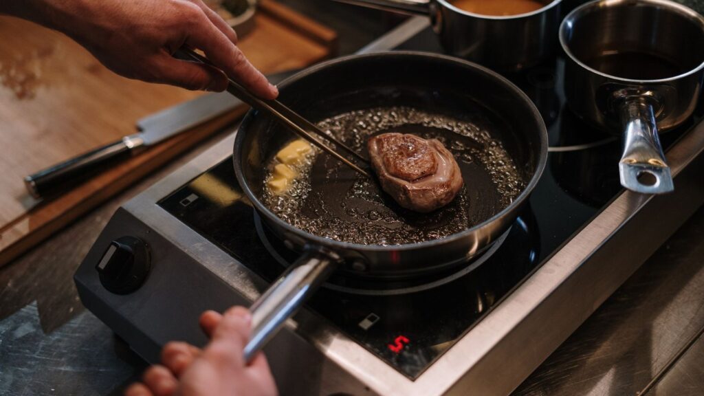 Pièce de viande qui saisit côté peau dans une poêle posée sur une plaque