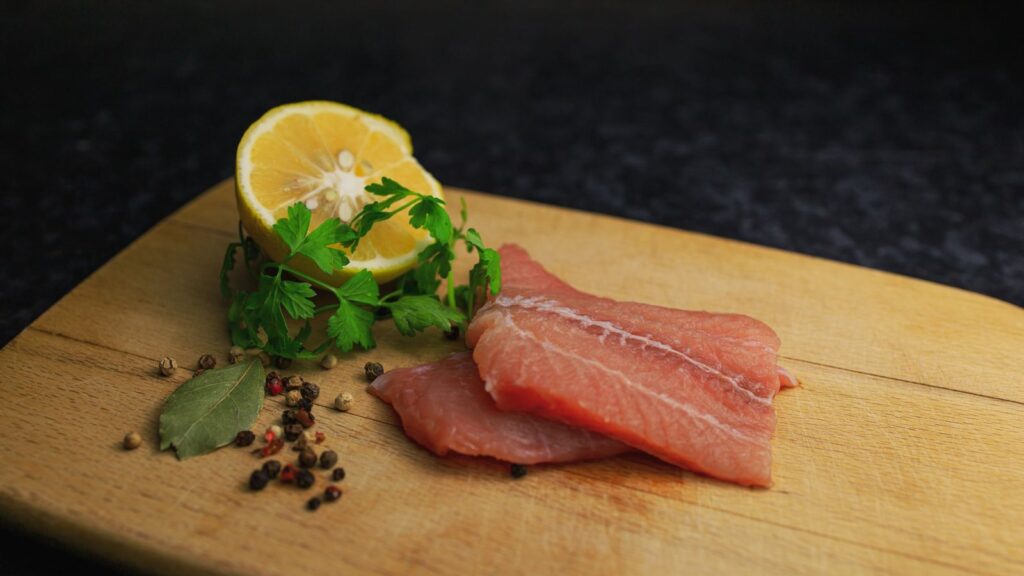 Filet de canard cru posé sur une planche avec un quartier de citron et des baies de poivre