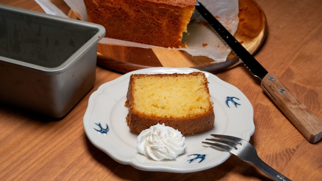 Tranche de cake posée sur une assiette à côté du moule à cake en métal