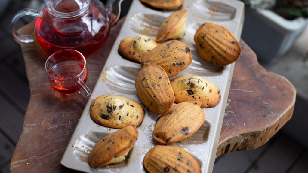 Madeleines alignées sur un plat, servies avec une théière et un verre de thé